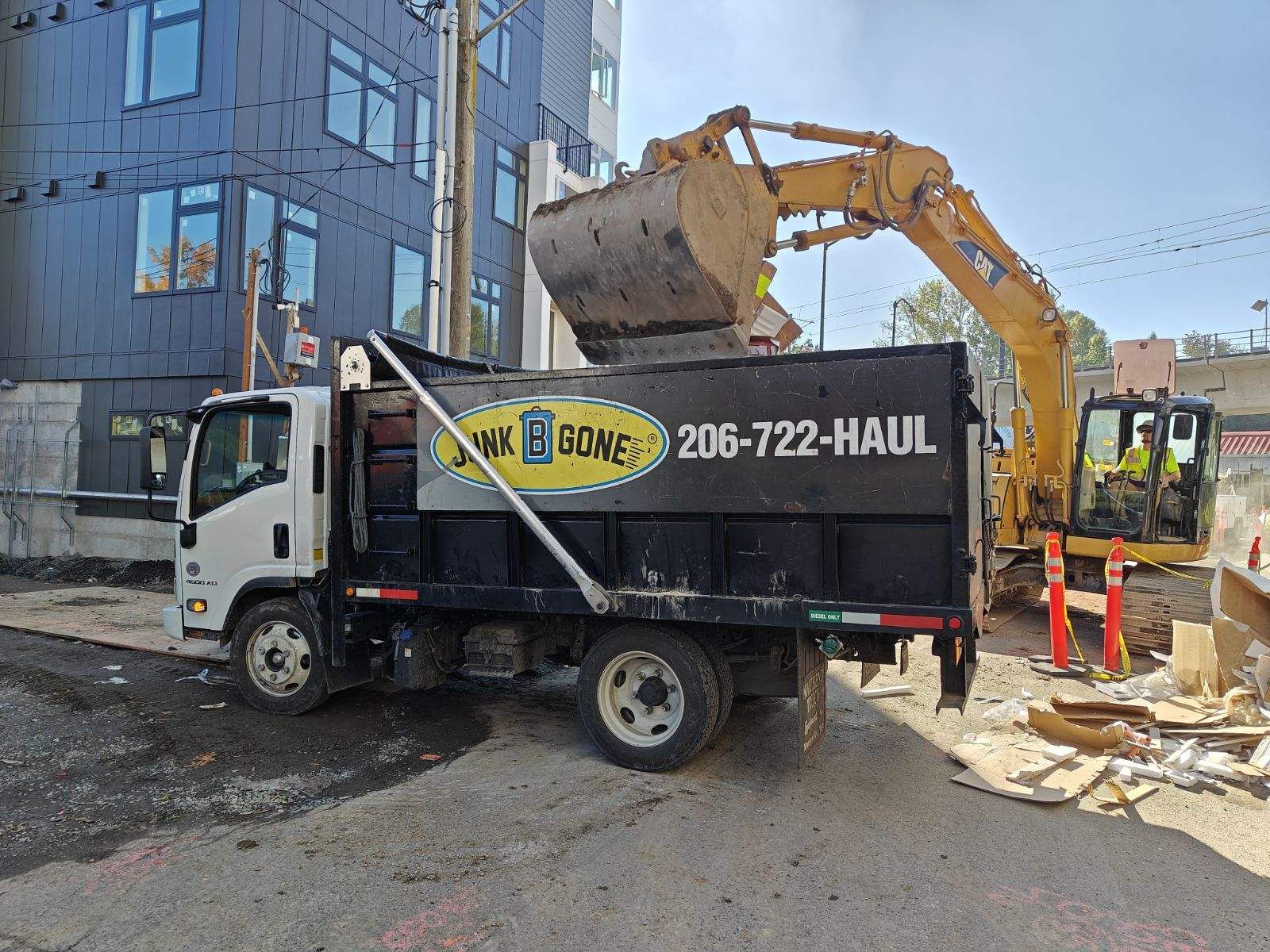 An excavator loads construction debris into a Junk B Gone truck at a Seattle job site