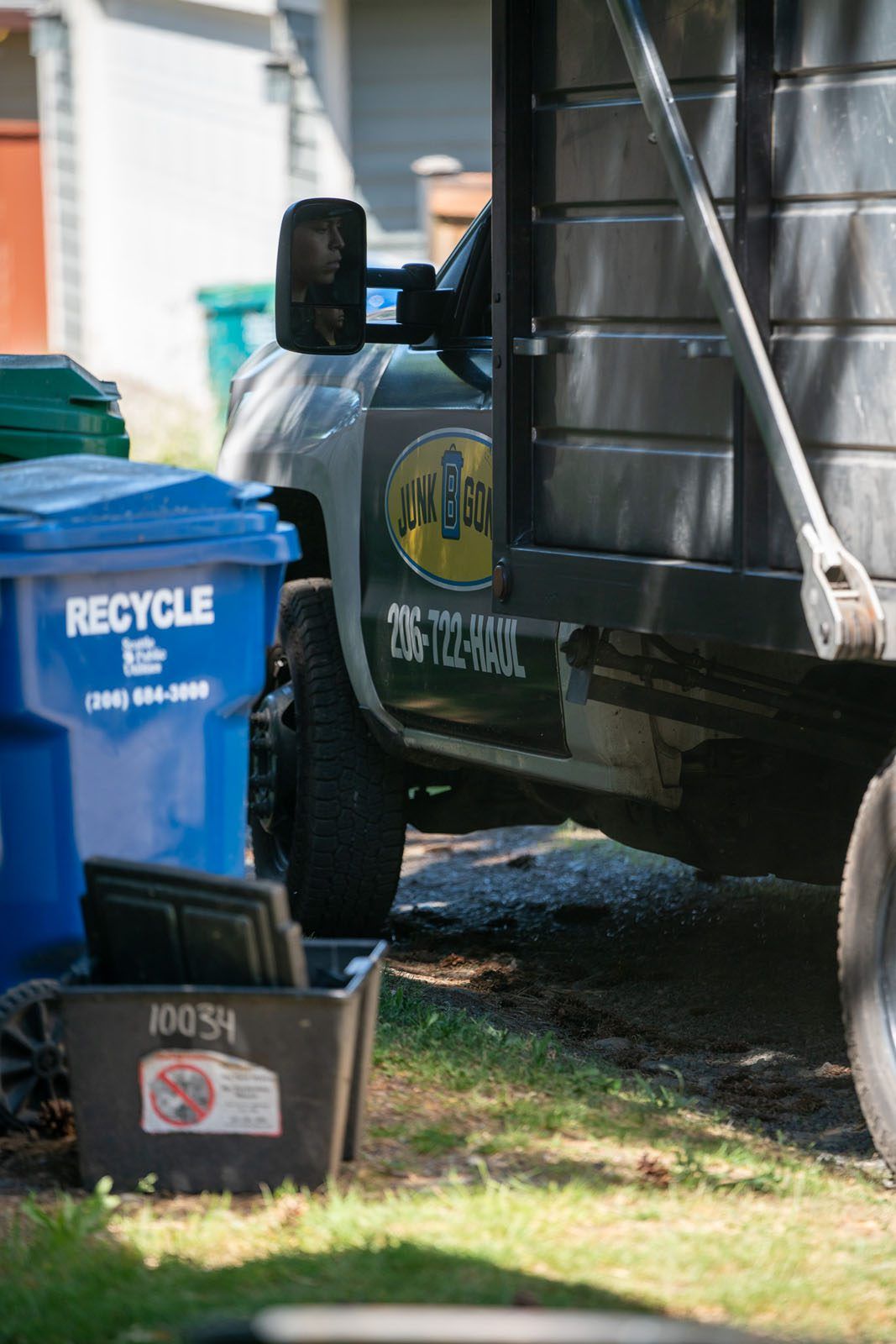 Junk B Gone truck parked beside a recycling bin on a residential street