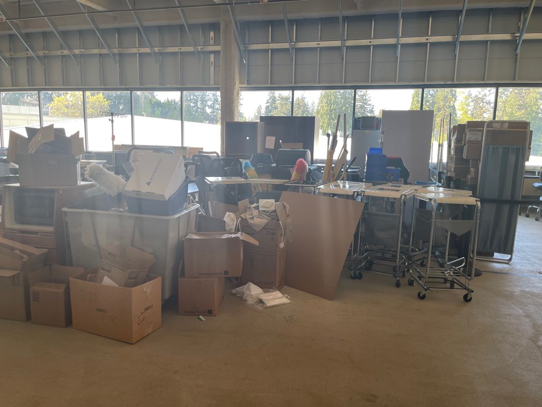 An open staging floor stacked with boxes, furniture and medical carts, before the cleanout.