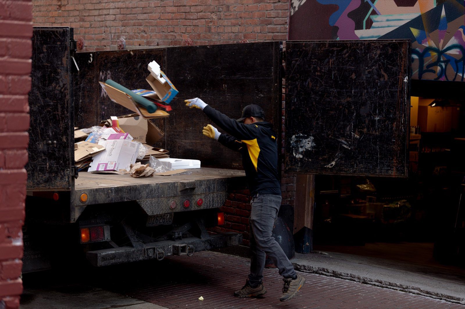 A Junk B Gone crew member loading boxes and debris into the bed of a branded work truck in a Seattle alley