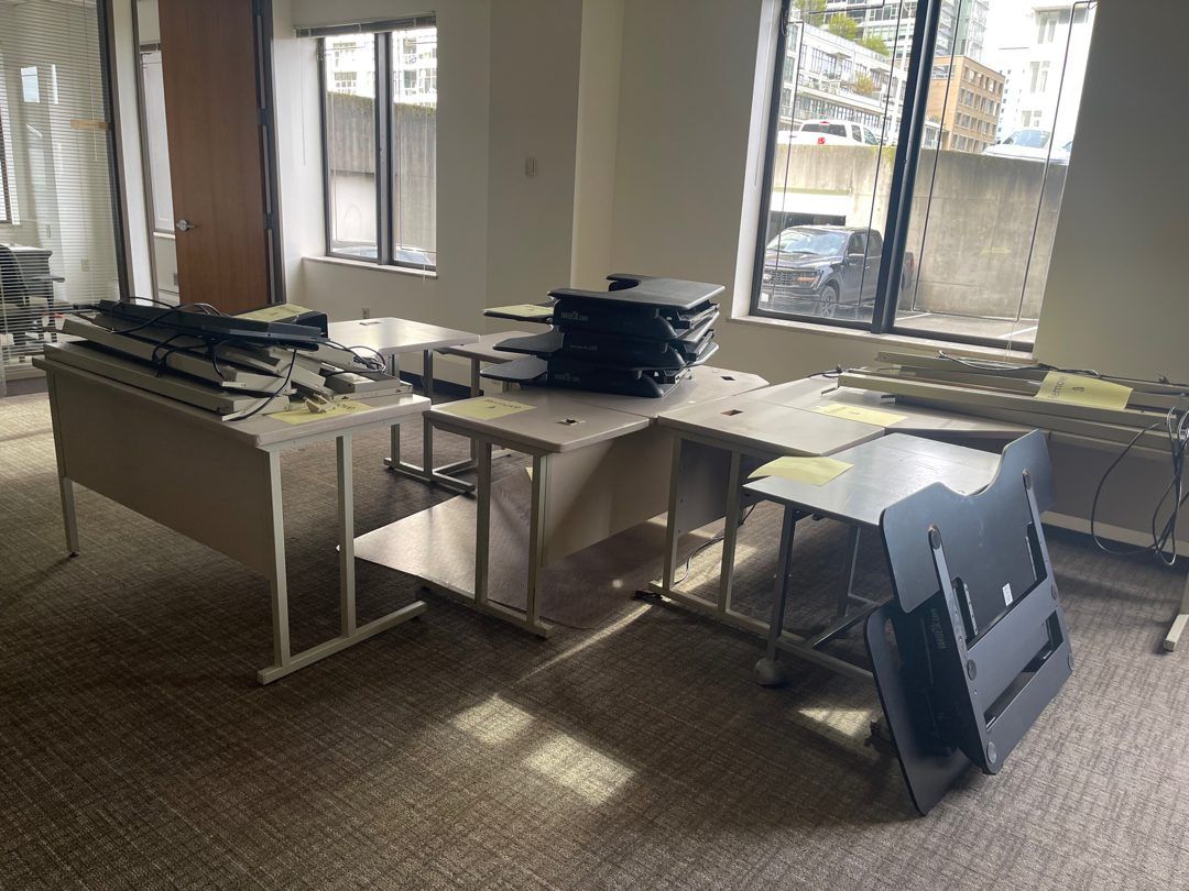 A Seattle office full of desks topped with stacked monitors and electronics, staged for Junk B Gone to haul out, city view through the windows