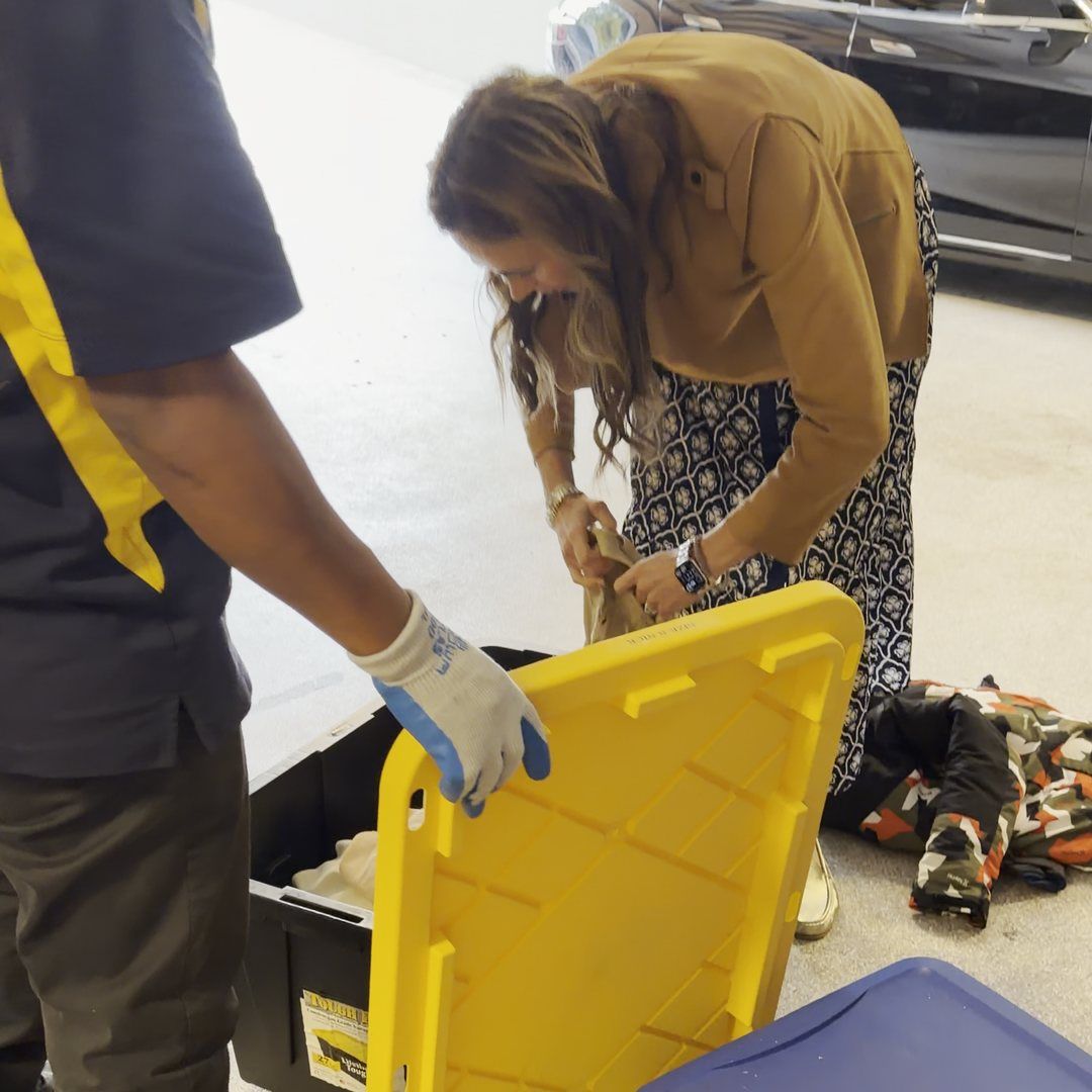 A Junk B Gone crew member and a homeowner sorting what stays and what goes at a yellow-lidded bin in a garage