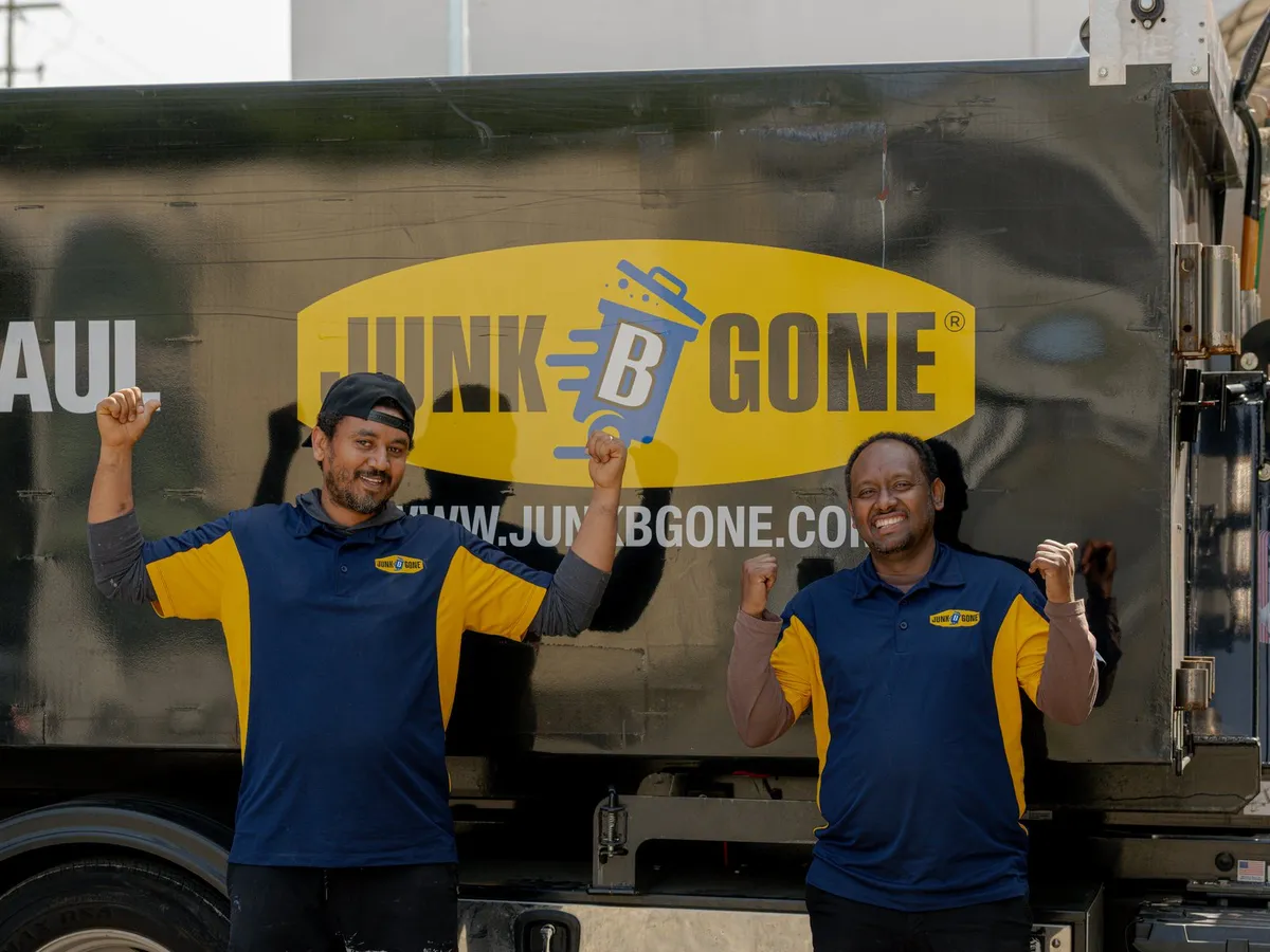 Two Junk B Gone crew members in company polos cheer in front of a company truck.