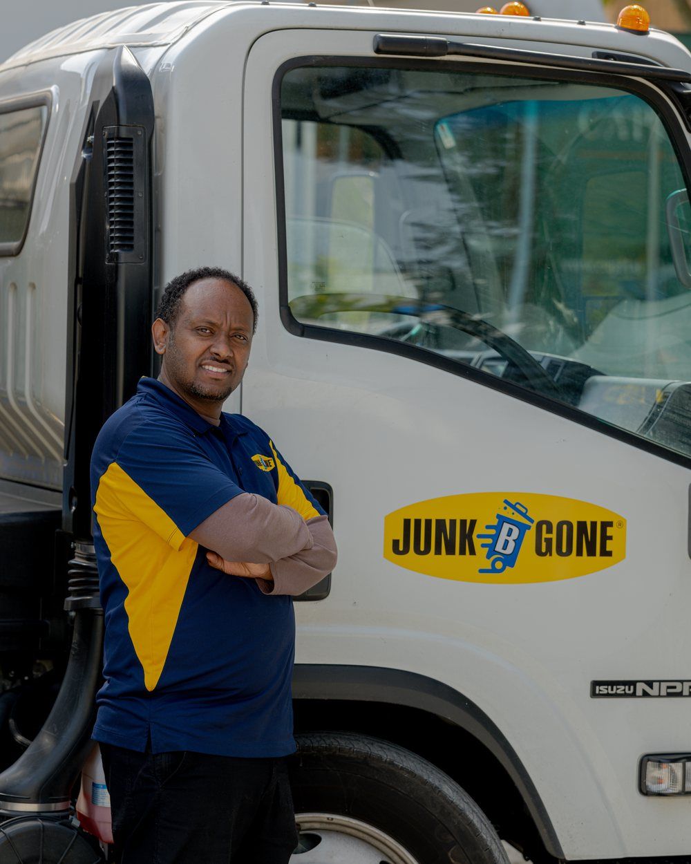 A Junk B Gone crew member in a company polo stands beside a company truck.