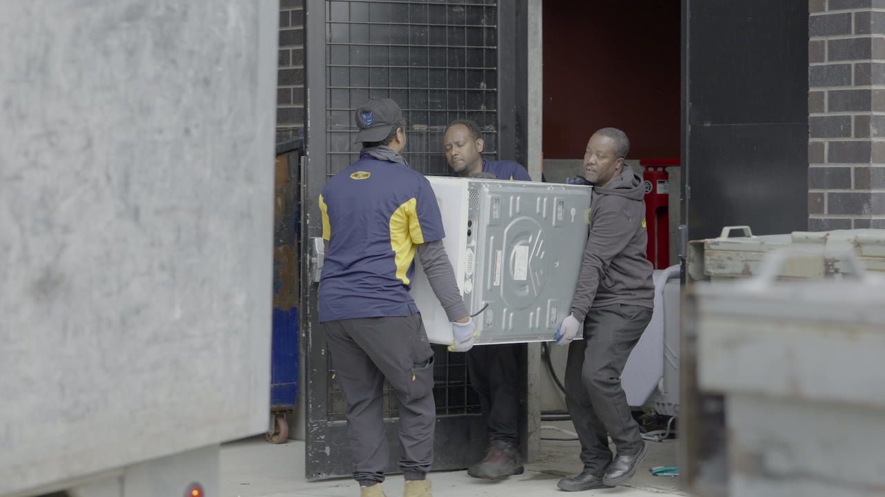 Three Junk B Gone crew members carry a washer through a building’s service door.