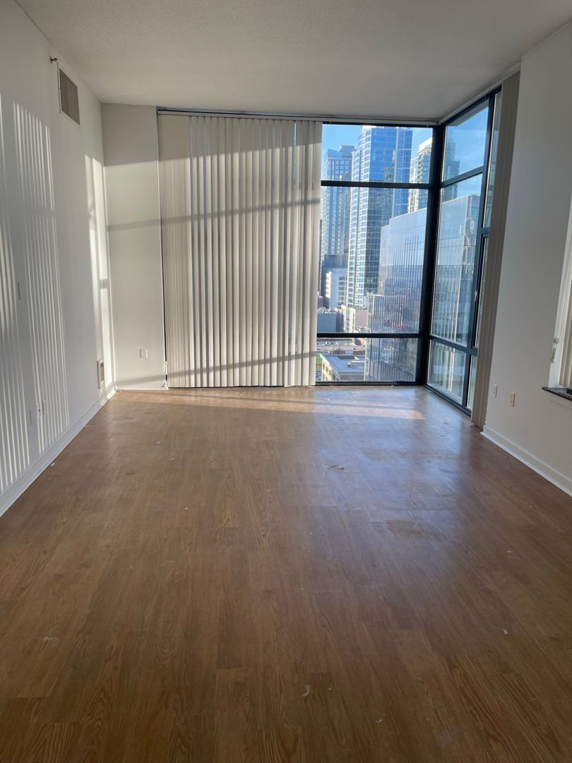 An empty apartment living room with floor-to-ceiling corner windows and downtown towers beyond, after the unit cleanout.
