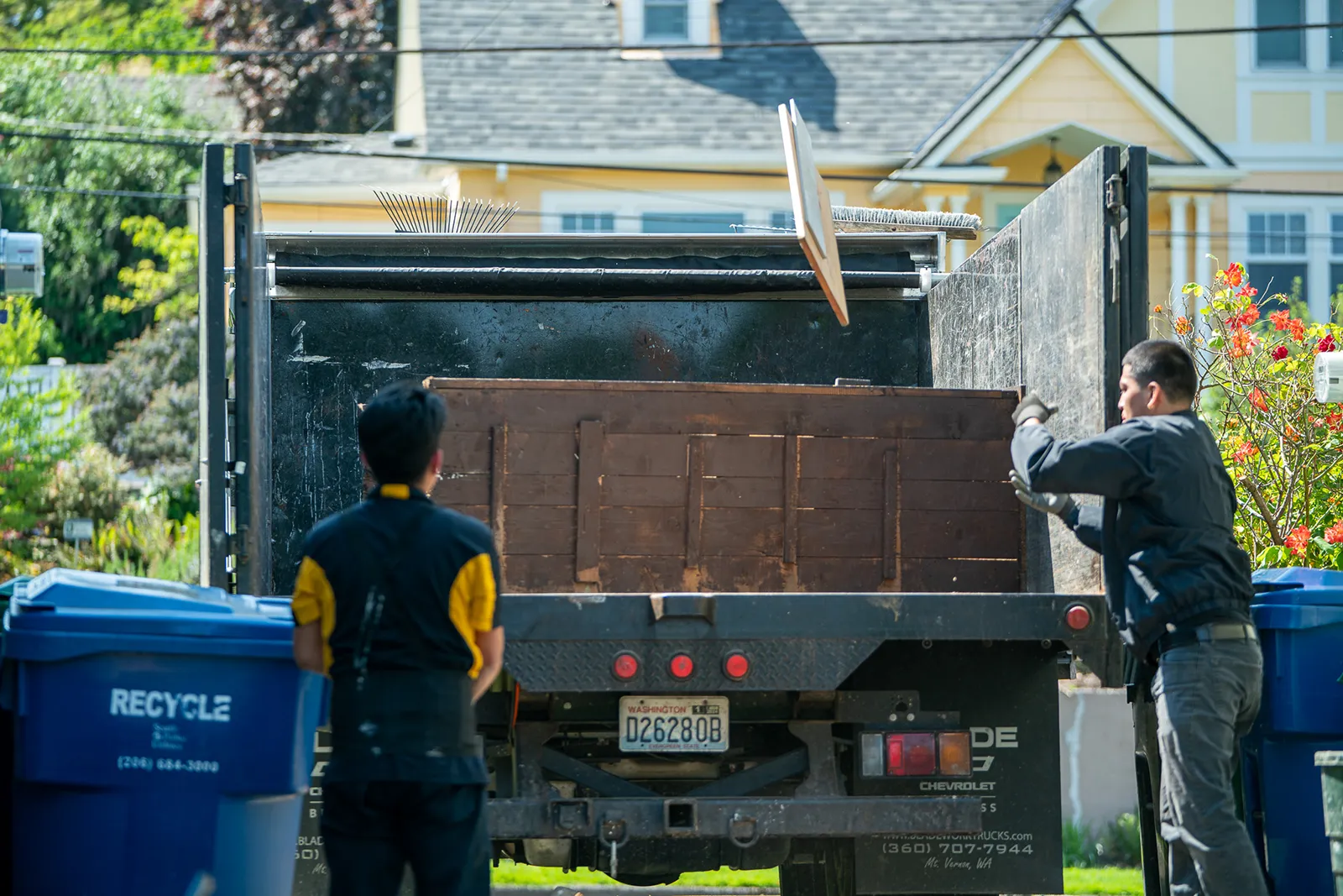 Two Junk Removal Seattle employees loading a bookcase furniture into the back of a junk removal truck