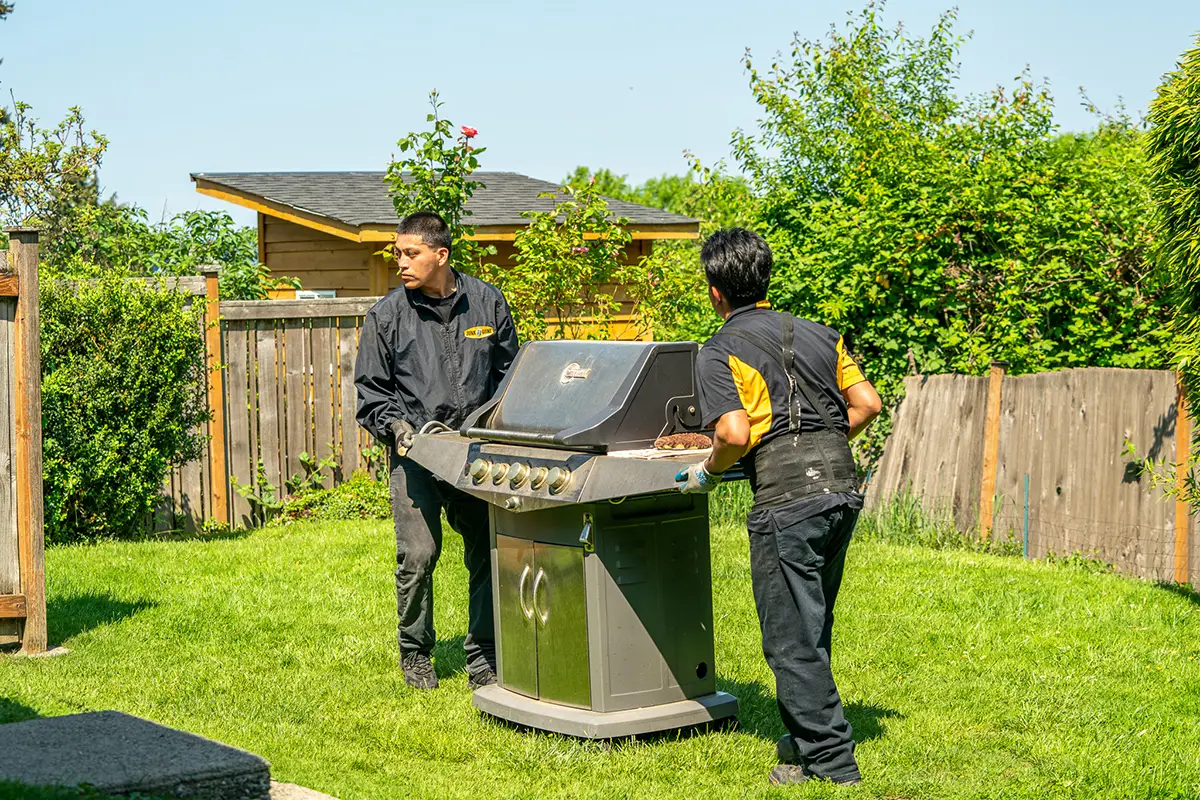Two Junk B Gone crew members picking up a BBQ grill from a sunny Seattle backyard