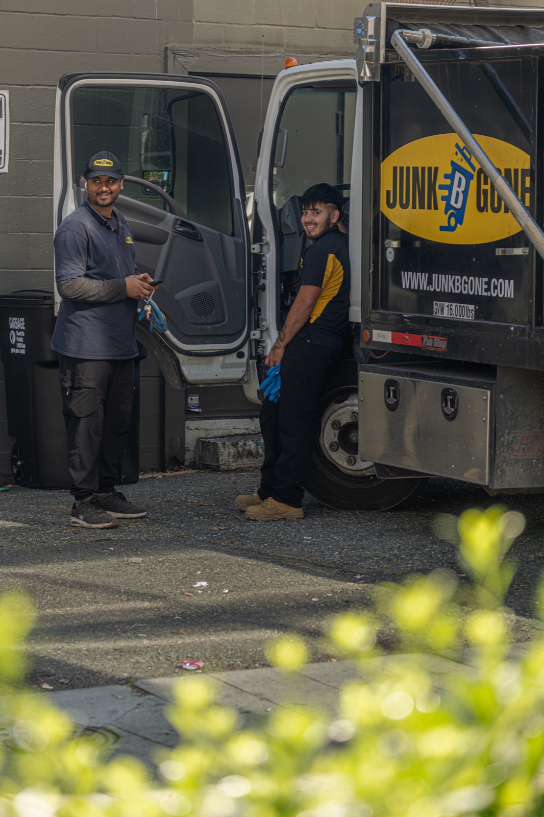 Two Junk B Gone crew members in branded uniforms standing by the truck